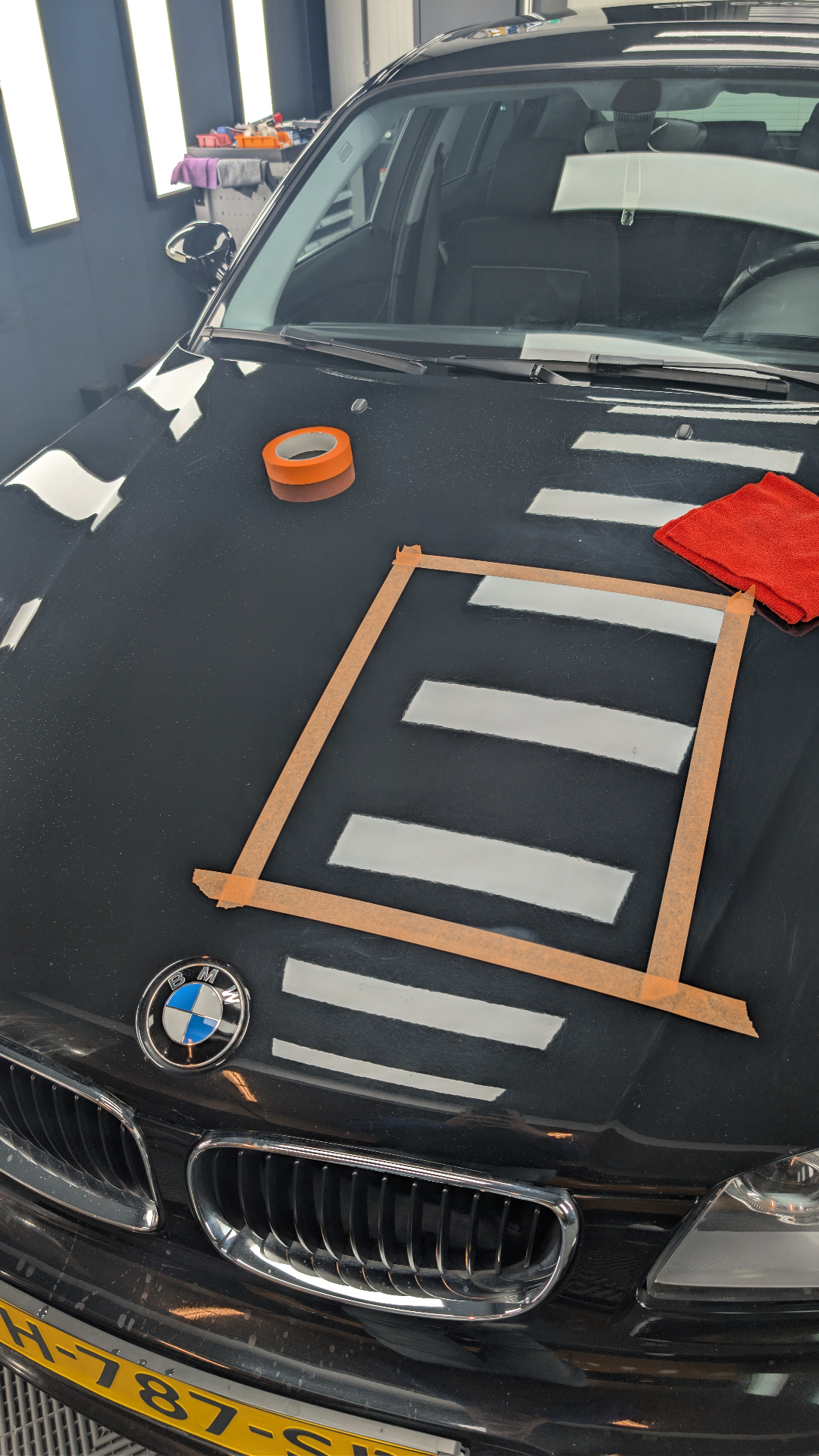 Testspot strak afgeplakt met oranje detailing tape op de motorkap van een BMW